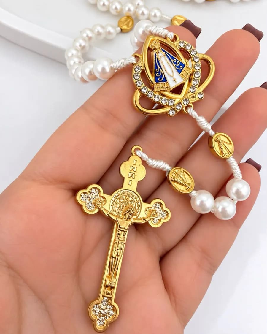 Terço de pérolas com crucifixo dourado e medalha de Nossa Senhora Aparecida na palma da mão